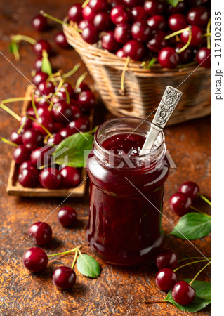 Cherry jam and fresh berries with leaves on an old brown table. 117102835