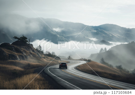 A lone car travels on a winding road through a foggy mountain landscape 117103684