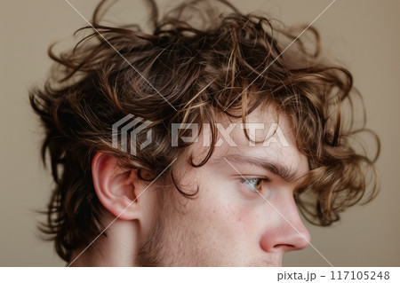 Close-up image of a young man's shaggy, curly hairstyle in a profile view with a neutral background 117105248