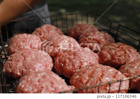 Raw minced meat for homemade grilled hamburgers. Several fresh and juicy hamburgers cooking on a fire grill 117106346