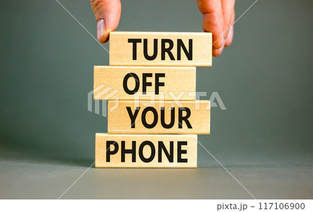 Turn off your phone symbol. Concept words Turn off your phone on wooden blocks. Beautiful grey table grey background. Businessman hand. Business psychological turn off your phone concept. Copy space 117106900