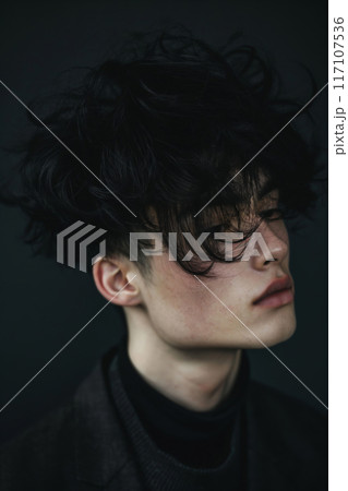 Moody close-up photo capturing a young man's messy fringe hairstyle against a dark background 117107536