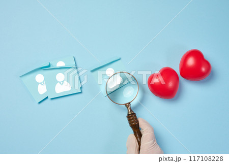 Female hand holding magnifying glass and red hearts on blue background, donor selection Female hand holding magnifying glass and red hearts on blue background, donor selection 117108228