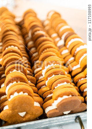 Making gingerbread man cookie sandwiches filled with eggnog buttercream, arrayed on a rustic wooden table, ideal for heartfelt Christmas gifting. 117108993