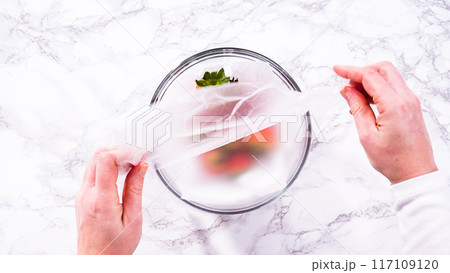 Flat lay. Strawberries, freshly washed and dried, are neatly stored in a glass bowl lined with a paper towel and securely covered with plastic wrap to maintain freshness. Flat lay. Strawberries, freshly washed and dried, are neatly stored in a glass bowl lined with a paper towel and securely covered with plastic wrap to maintain freshness. 117109120