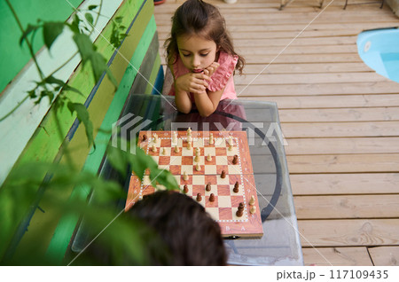 Little girl concentrating on a chess game outdoors 117109435