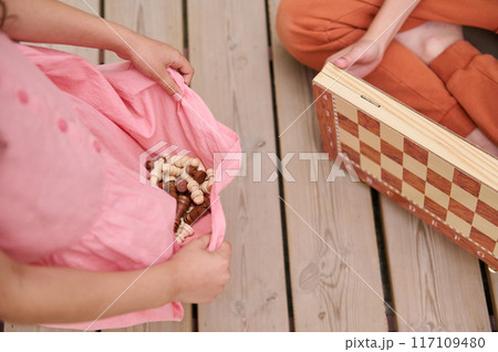 Children playing chess on wooden floor, holding pieces in dress Children playing chess on wooden floor, holding pieces in dress 117109480
