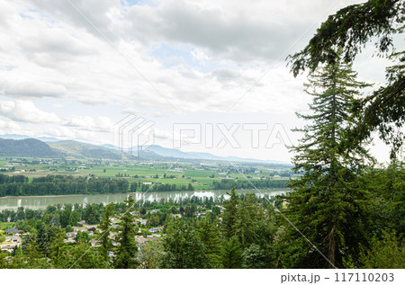View of the Mission town with Fraser River, lush green valley and the mountains in the background - Fraser Valley, BC, Canada 117110203