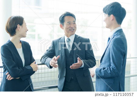 オフィスの廊下で雑談をするビジネスパーソン オフィスの廊下で雑談をするビジネスパーソン 117110357