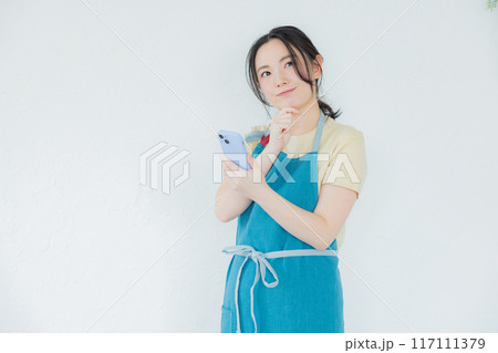 スマホを見るエプロンの女性 117111379