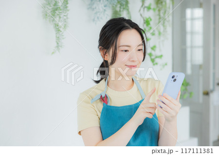 スマホを見るエプロンの女性 117111381