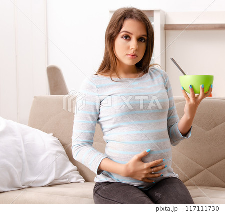 Young pregnant woman sitting on the sofa at home Young pregnant woman sitting on the sofa at home 117111730
