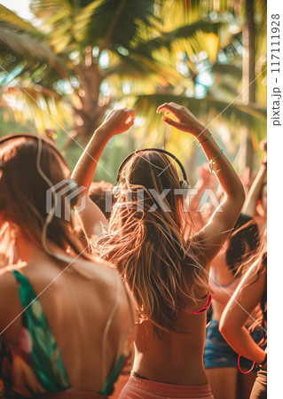 A group of people are dancing in the sun, with one woman wearing headphones 117111928