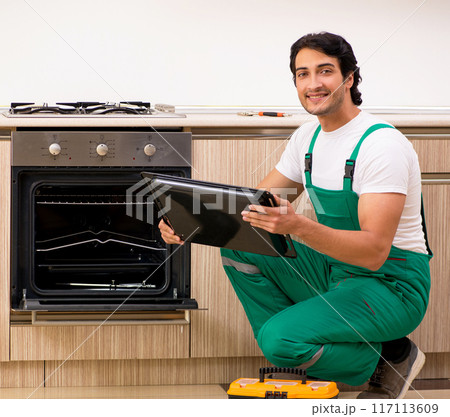 Young contractor repairing oven in kitchen 117113609