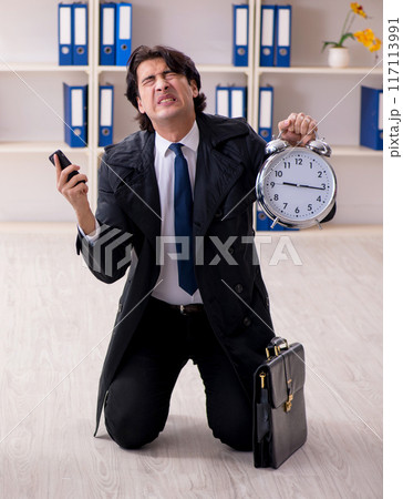 Young male employee in the office in time management concept Young male employee in the office in time management concept 117113991