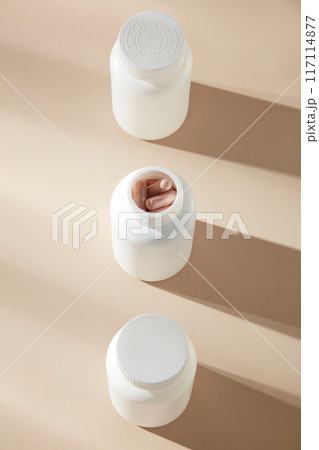 Top shot at the beige flat displaying some white unlabeled vitamin bottles, which arranged as a straight line, the bottle in center is opened with some purple vitamin capsule inside 117114877