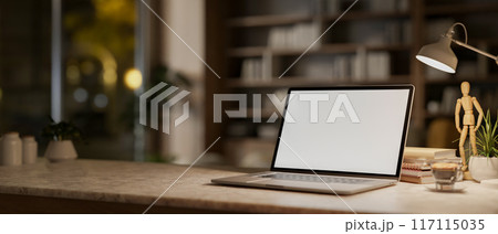 A laptop computer on a table in a modern room at night, illuminated by a table lamp. 117115035