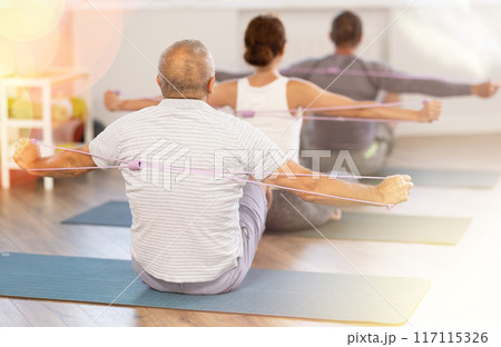 Group of men and women exercising with pilates loop back view Group of men and women exercising with pilates loop back view 117115326