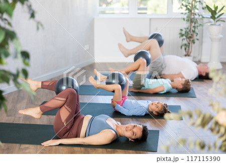 Willing middle-aged woman lying on the floor holding softball between legs with her family Willing middle-aged woman lying on the floor holding softball between legs with her family 117115390