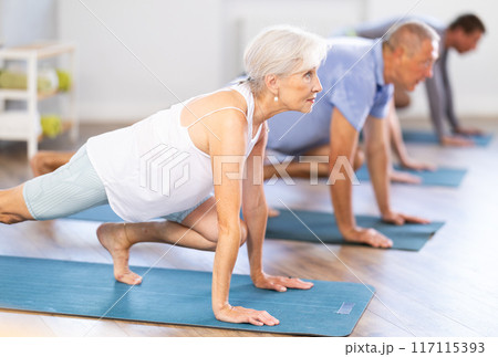 Diligent women and men doing body stretching before yoga class in a fitness studio Diligent women and men doing body stretching before yoga class in a fitness studio 117115393