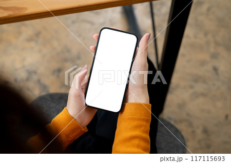 A woman sitting indoors and using her smartphone. a smartphone with a white-screen mockup. 117115693