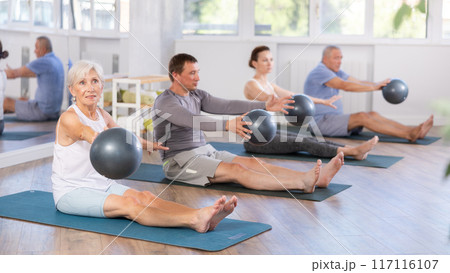 Sitting on floor, mature woman with class participants move soft ball around torso Sitting on floor, mature woman with class participants move soft ball around torso 117116107