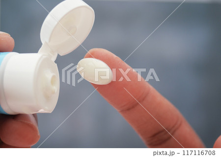 Applying cream from a tube onto a finger for skincare and beauty purposes is essential 117116708
