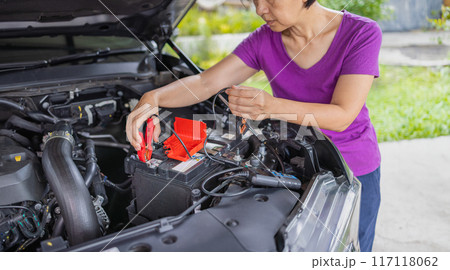 Senior Woman is jumping charger cable to AGM battery on car. 117118062