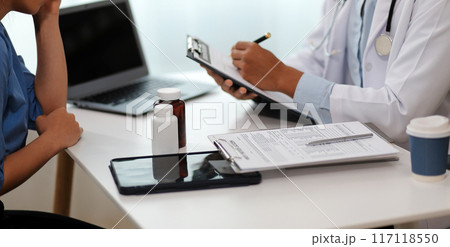 Doctor and patient sitting near each other at the wooden desk in clinic. Female physician's pointing to a records form. Medicine concept Doctor and patient sitting near each other at the wooden desk in clinic. Female physician's pointing to a records form. Medicine concept 117118550