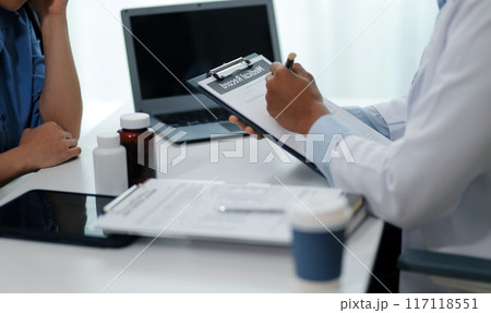 Doctor and patient sitting near each other at the wooden desk in clinic. Female physician's pointing to a records form. Medicine concept Doctor and patient sitting near each other at the wooden desk in clinic. Female physician's pointing to a records form. Medicine concept 117118551