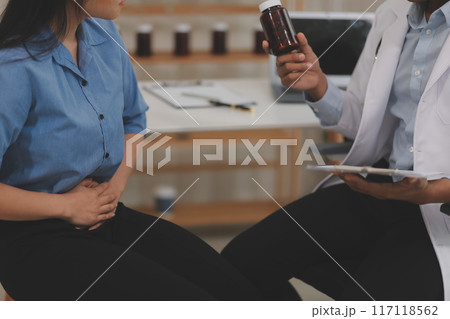 Confident doctor man holding a pill bottle and writing while talking with senior patient and reviewing his medication at office room. 117118562
