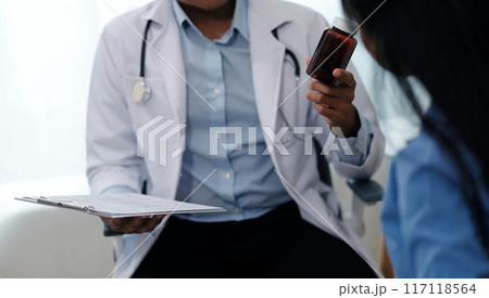 Confident doctor man holding a pill bottle and writing while talking with senior patient and reviewing his medication at office room. 117118564
