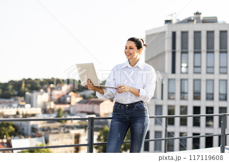 Confident businesswoman working on laptop outdoors on rooftop Confident businesswoman working on laptop outdoors on rooftop 117119608