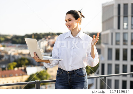 Remote business meeting on rooftop with happy woman using laptop 117119634