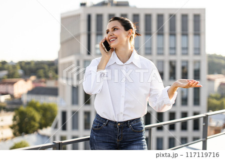 Smiling woman on phone call outside modern office building 117119716
