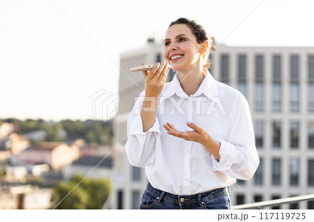 Happy woman using smartphone voice assistant on rooftop terrace 117119725