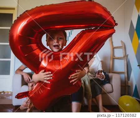 Little boy with big red inflatable number 4 celebrates his birthday with his family 117120382