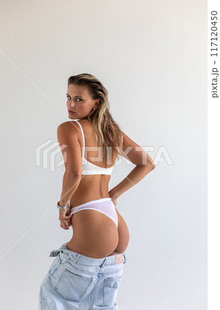 Beautiful blonde takes off her jeans on a white background 117120450