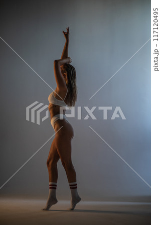Beautiful athletic girl in socks and underwear posing in a photo studio. Dramatic light. Vertical photographs. 117120495