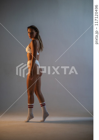Beautiful athletic girl in socks and underwear posing in a photo studio. Dramatic light. Vertical photographs. 117120496