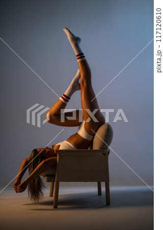 A beautiful athletic girl in socks and underwear lies on a chair. Dramatic light. 117120610