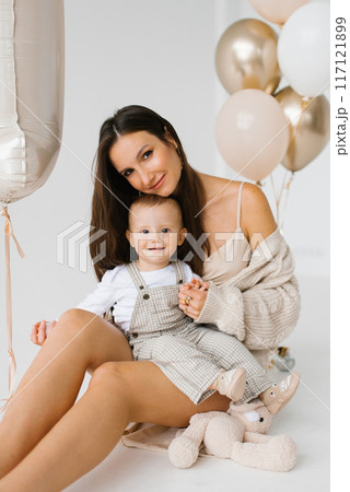 Portrait of a caucasian mother and a one-year-old baby celebrating their birthday with balloons Portrait of a caucasian mother and a one-year-old baby celebrating their birthday with balloons 117121899