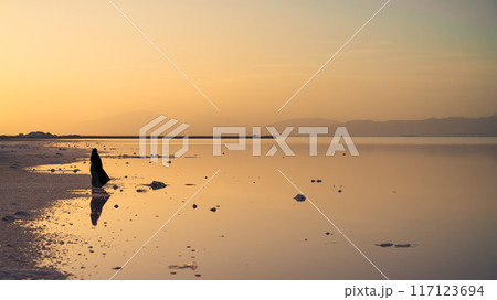 Maharloo pink lake during sunset with a veiled Iranian woman in hijab black dress by the lake coast, Iran Maharloo pink lake during sunset with a veiled Iranian woman in hijab black dress by the lake coast, Iran 117123694