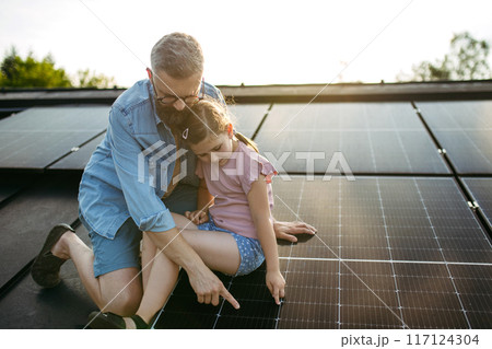 Dad and girl on roof with solar panels, learning about solar energy. Rooftop solar or photovoltaic system. Sustainable future for next generation. 117124304
