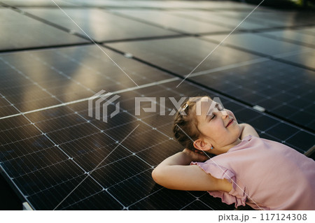 Cute girl lying on solar panels roof, shot with copy space. Rooftop solar or photovoltaic system. Sustainable future for next generation. Cute girl lying on solar panels roof, shot with copy space. Rooftop solar or photovoltaic system. Sustainable future for next generation. 117124308