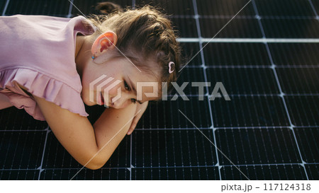 Cute girl lying on solar panels roof, shot with copy space. Rooftop solar or photovoltaic system. Sustainable future for next generation. 117124318
