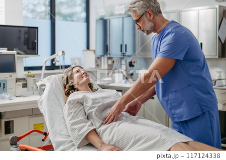 Doctor palpating woman's abdomen, using hands and steady pressure. 117124338