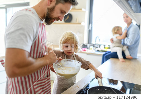 Young nuclear family making pancakes together. Parents and children in kitchen, preparing pancake batter, spending weekend day indoors. 117124990
