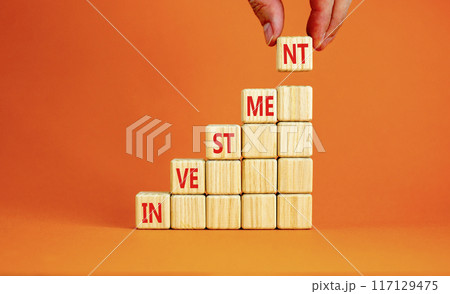 Investment symbol. Concept word Investment on beautiful wooden cubes. Beautiful orange background. Businessman hand. Business investment concept. Copy space. 117129475