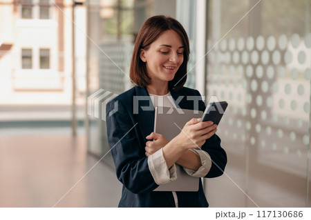 A young professional woman is seen using a smartphone in a modern office setting A young professional woman is seen using a smartphone in a modern office setting 117130686
